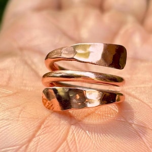 Op de afbeelding: Een koperen ring met een gehammerde afwerking. De ring is gemaakt van drie banden die met elkaar zijn gedraaid. De ring is een eenvoudig en elegant ontwerp.
