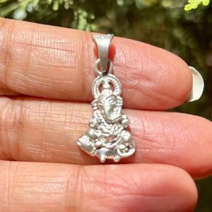 May include: Silver pendant featuring a detailed depiction of the Hindu deity Ganesha. The pendant is intricately crafted with a three-dimensional design, showcasing Ganesha's trunk, large ears, and other distinctive features.