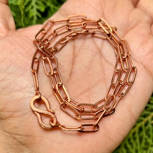 Puede incluir: Un collar de cadena de cobre con cierre de mosquetón. La cadena está hecha de pequeñas formas ovaladas enlazadas.