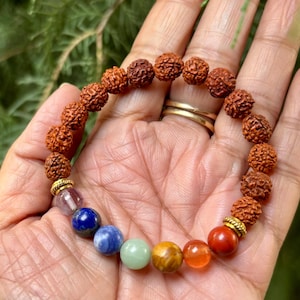 May include: A colourful beaded bracelet with a mix of brown, orange, blue, green, and purple gemstones. The bracelet includes textured brown beads and a variety of smooth, colourful gemstones. The bracelet is designed for spiritual or fashion purposes.