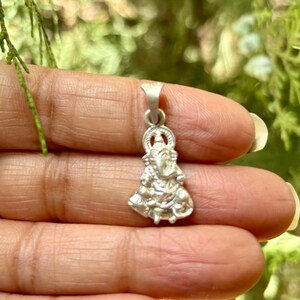 May include: A silver pendant featuring a detailed depiction of a Hindu deity. The pendant is intricately crafted with fine details and a traditional design.