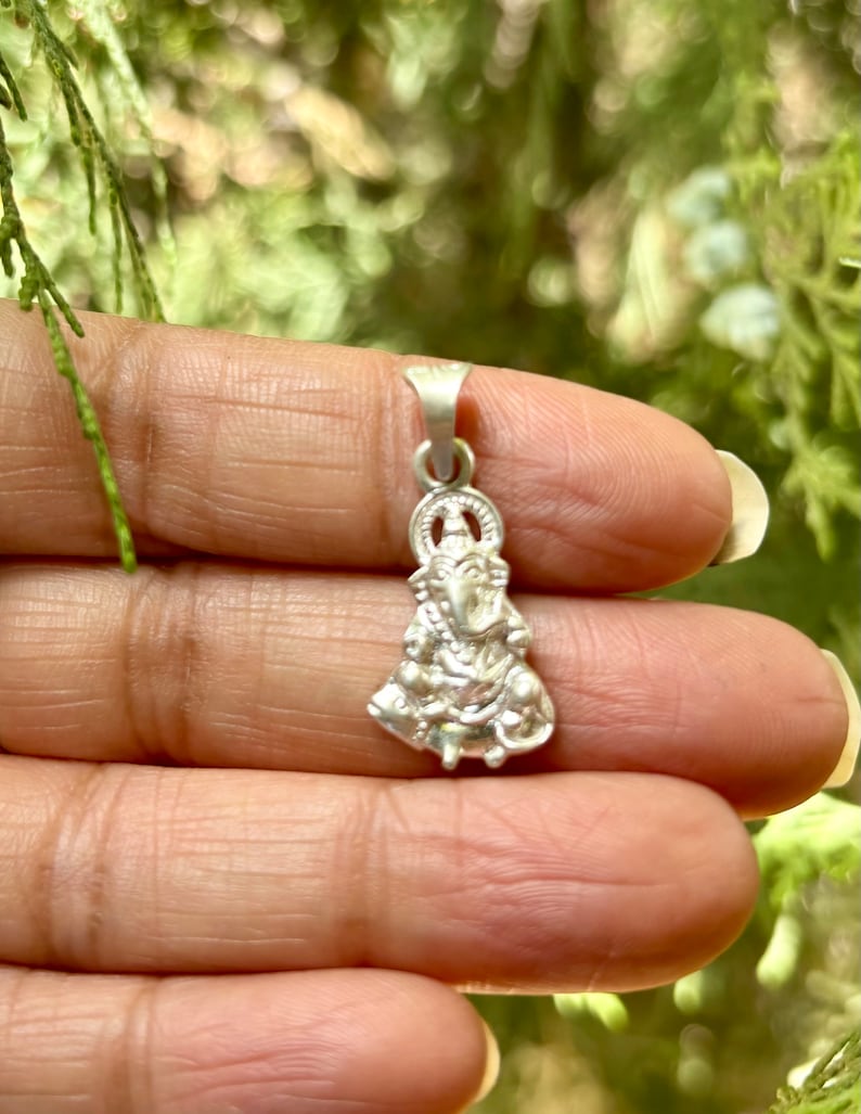 May include: A silver pendant featuring a detailed depiction of a Hindu deity. The pendant is intricately crafted with fine details and a traditional design.