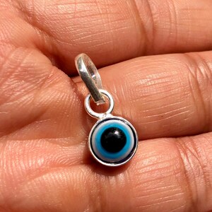 Puede incluir: Un amuleto de plata con un dise&ntilde;o de ojo turco azul. El amuleto es redondo y tiene un bucle de plata en la parte superior para sujetarlo a un collar o pulsera.