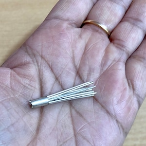 May include: A silver-coloured metal object with a cylindrical base and multiple thin, pointed strands extending from the top. The object is held in a person's hand.