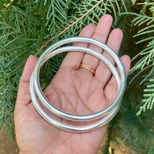 May include: Two silver bangle bracelets stacked on top of each other. The bracelets are smooth and round.