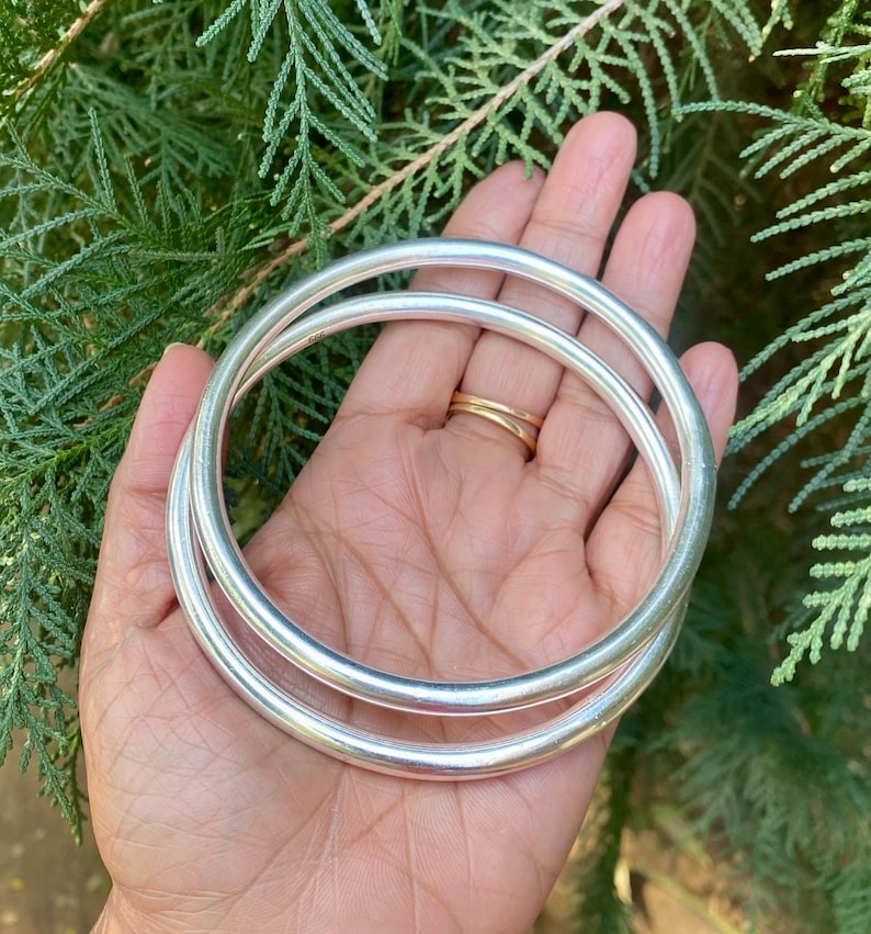 May include: Two silver bangle bracelets stacked on top of each other. The bracelets are smooth and round.