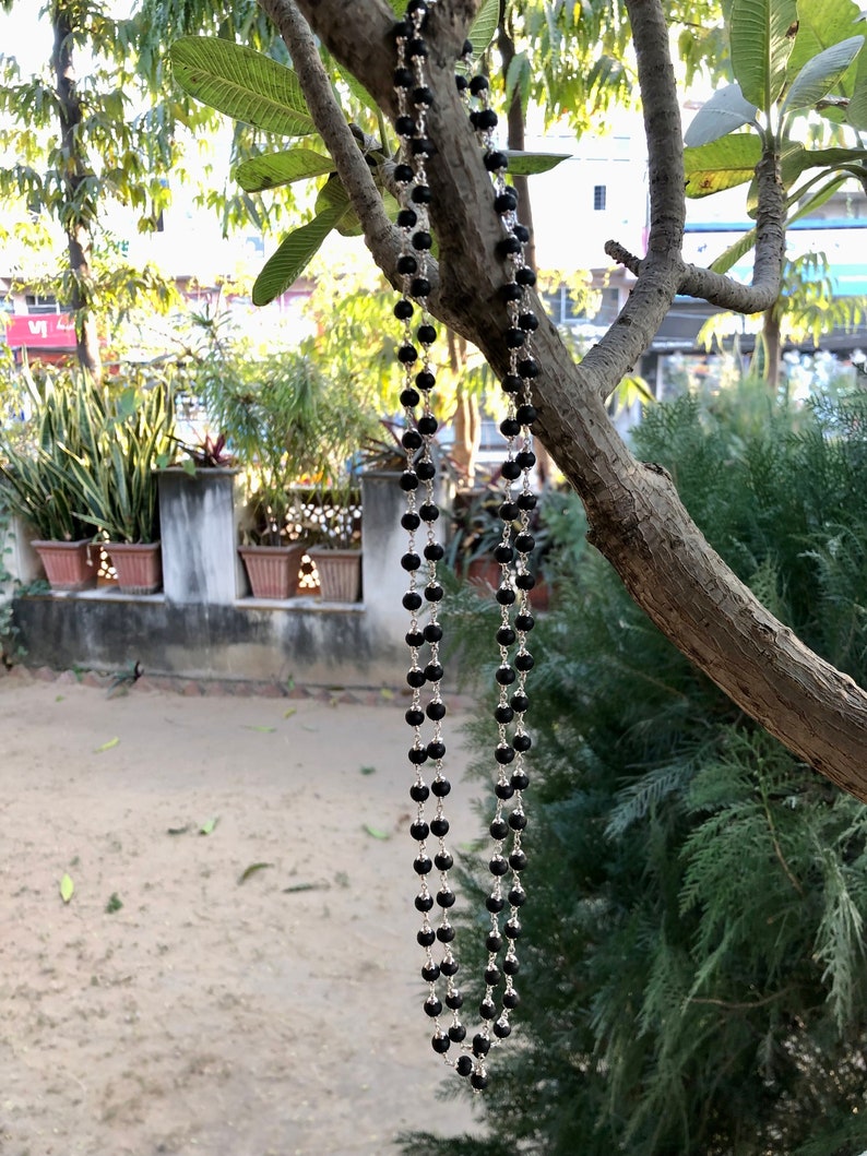 May include: A black beaded necklace with silver accents hanging from a tree branch.