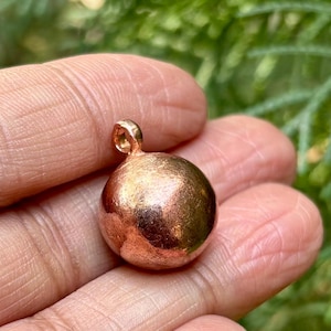 Peut inclure: Un petit pendentif rond de couleur cuivre avec une boucle en haut pour l'attacher à une chaîne ou un cordon.