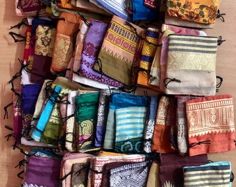 May include: A collection of colorful fabric drawstring pouches with various patterns and designs. The pouches are made from recycled sari fabric and are perfect for storing small items like jewelry, coins, or gifts.