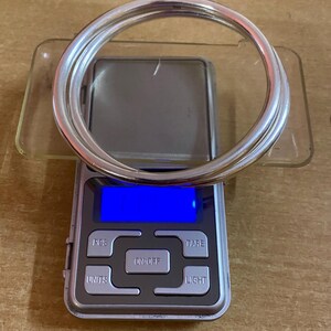 May include: Two silver bangles on a digital scale with a blue display. The scale has buttons labeled "PCS", "TARE", "ON/OFF", "UNITS", and "LIGHT".
