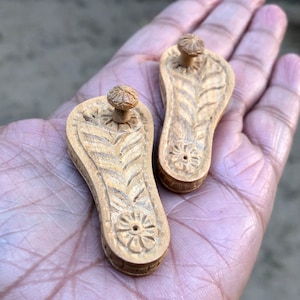 Pu&ograve; includere: Due piccole sandali di legno intagliate con un motivo floreale. Le sandali sono di colore marrone chiaro e hanno un piccolo pomo nella parte superiore.