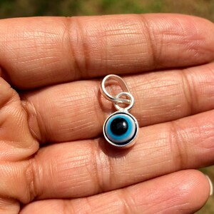 Puede incluir: Un amuleto de plata con un dise&ntilde;o de ojo azul malvado. El amuleto tiene un bucle en la parte superior para sujetarlo a un collar o pulsera.