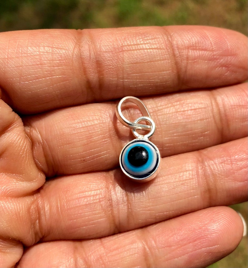 Puede incluir: Un amuleto de plata con un dise&ntilde;o de ojo azul malvado. El amuleto tiene un bucle en la parte superior para sujetarlo a un collar o pulsera.