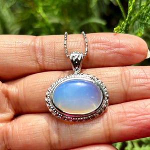 May include: A silver chain necklace with a silver oval pendant featuring a light blue opal gemstone.