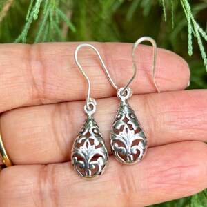 May include: A pair of silver filigree teardrop earrings with a delicate floral design.