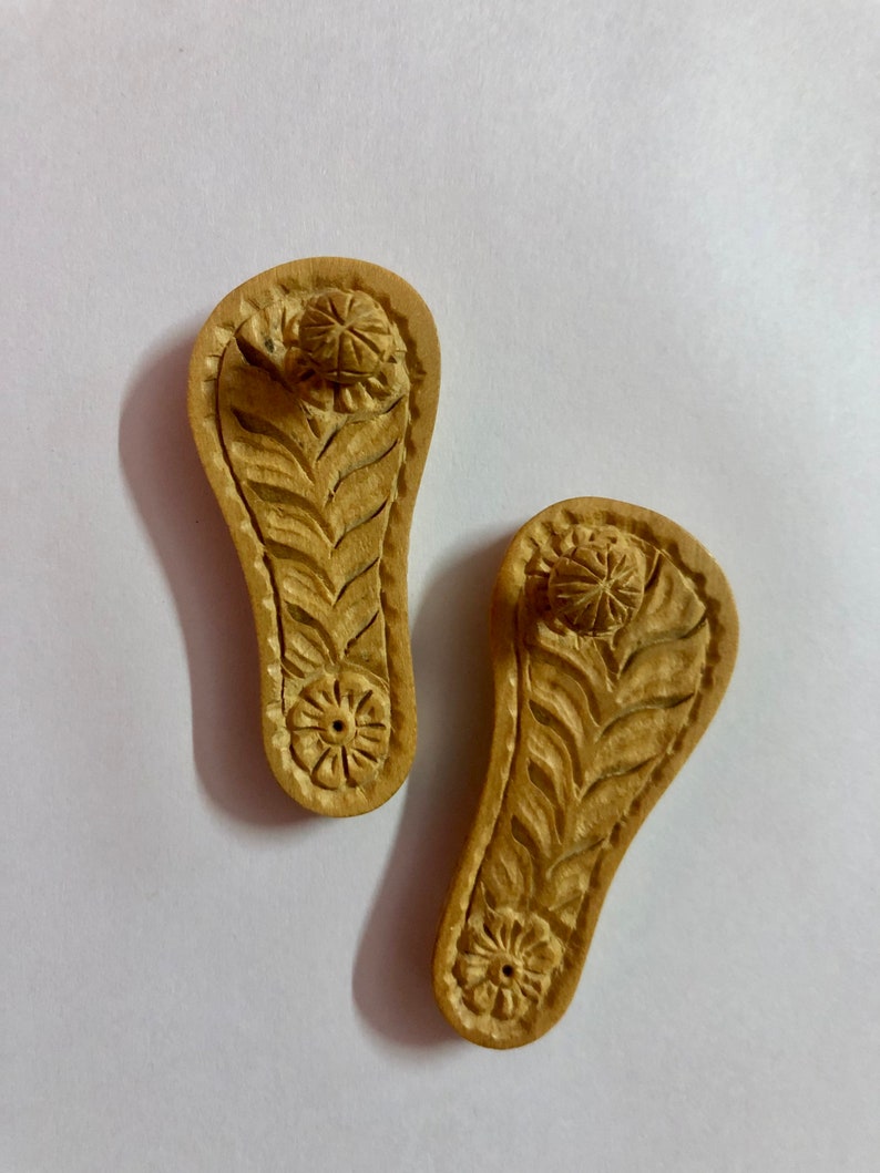 Pu&ograve; includere: Due porta incensi in legno a forma di sandali con intricate sculture di fiori e foglie. I supporti hanno un piccolo foro nella parte superiore per i bastoncini di incenso.