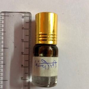 Puede incluir: Una pequeña botella de vidrio transparente con una tapa dorada y una etiqueta blanca. La etiqueta tiene el texto "फूलजली" escrito en tinta negra.