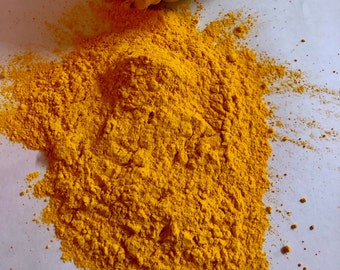 May include: A pile of bright yellow turmeric powder on a white surface.