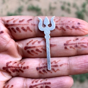 May include: A silver trident charm with a three-pronged design. The charm is small and delicate, and would be perfect for adding a touch of spirituality to a necklace or bracelet.