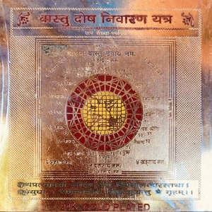 Può includere: Una placca di metallo placcato oro con un design circolare rosso e oro al centro. La placca ha testo in hindi, tra cui le parole "Vastu Dosh Nivaran Yantra" e "24K Gold Plated".