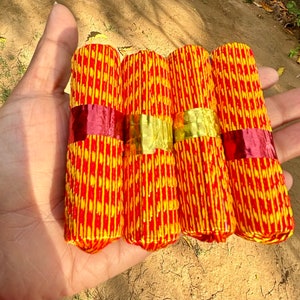 May include: Four red and yellow incense sticks wrapped in decorative paper. The paper has a repeating pattern of red and yellow stripes.