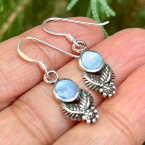 Può includere: Un paio di orecchini in argento con pietre cabochon azzurre incastonate in un design a foglie dettagliato. Gli orecchini hanno una chiusura a gancio.