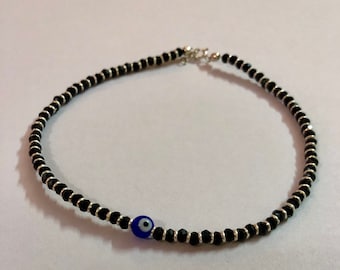 May include: A black beaded anklet with a silver clasp and a blue evil eye charm.