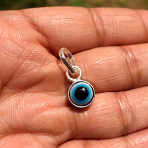 Puede incluir: Un amuleto de plata con un dise&ntilde;o de ojo azul malvado. El amuleto tiene un bucle en la parte superior para sujetarlo a una pulsera o collar.
