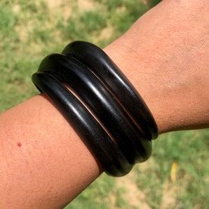 May include: A set of three black bangle bracelets made of polished wood.