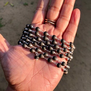 May include: A black beaded necklace with silver chain links. The necklace is folded in a hand.