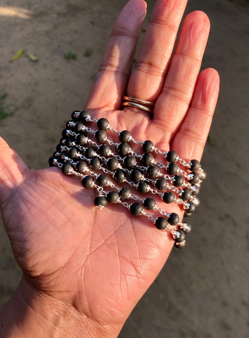 May include: A black beaded necklace with silver chain links. The necklace is folded in a hand.