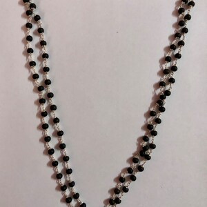 May include: A black beaded necklace with a silver chain. The necklace is made of round beads and is approximately 18 inches long.