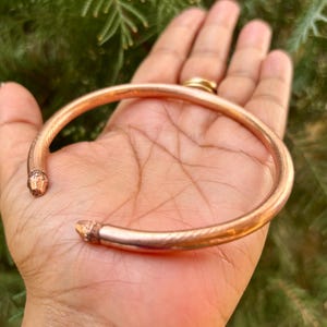 May include: A copper bangle bracelet with a hammered finish. The bracelet is open and has pointed ends.