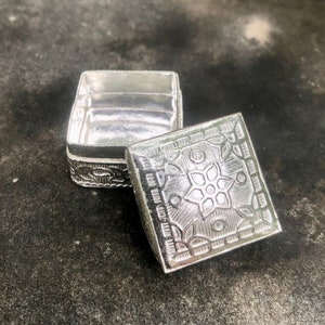 Puede incluir: Una caja cuadrada de plata con un intrincado diseño floral en la tapa. La caja está abierta y el interior está vacío.