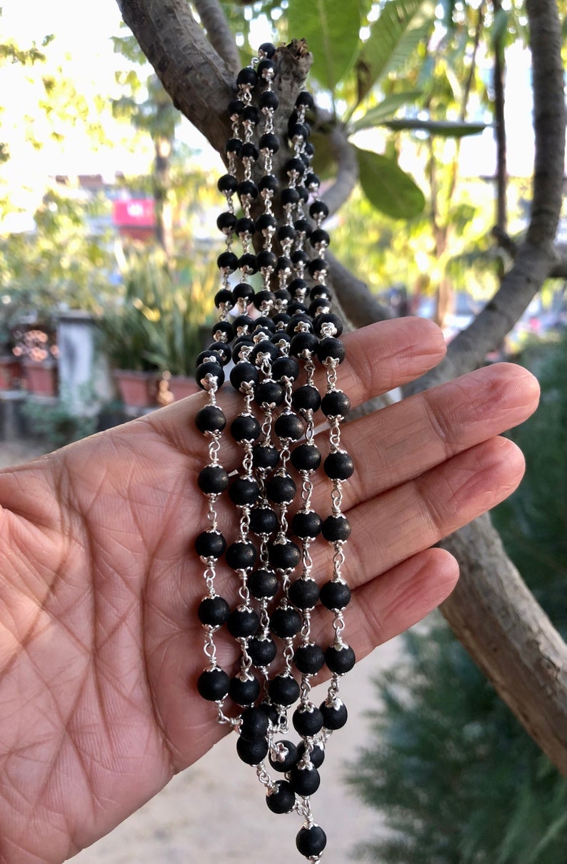 May include: A black beaded necklace with silver chain links. The necklace is made of multiple strands of beads and is hanging from a hand.
