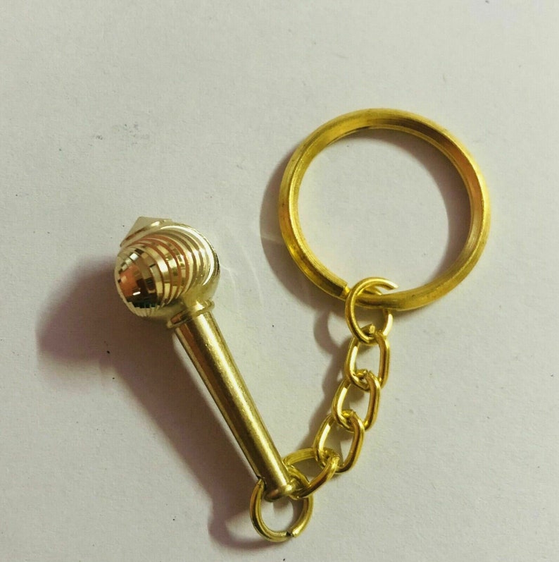 May include: A gold-coloured keychain with a decorative, round, textured charm attached to a gold chain and ring.