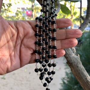 May include: A black beaded necklace with silver chain accents. The necklace is layered and has a cascading effect.