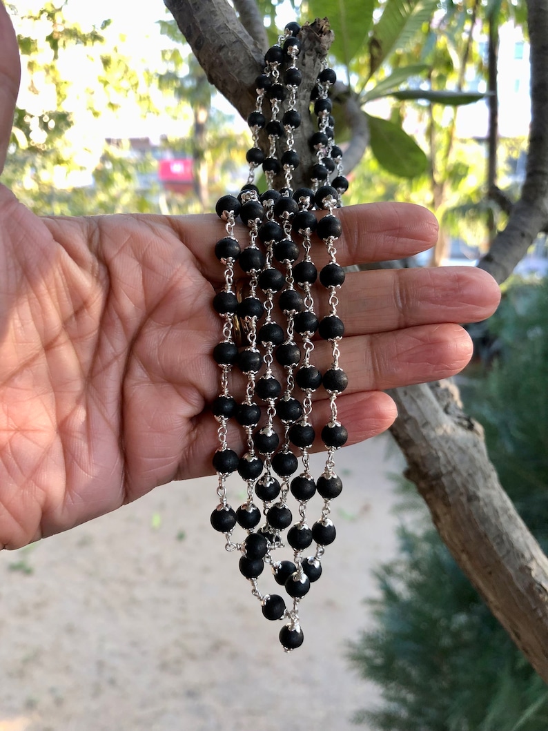 May include: A black beaded necklace with silver chain accents. The necklace is layered and has a cascading effect.