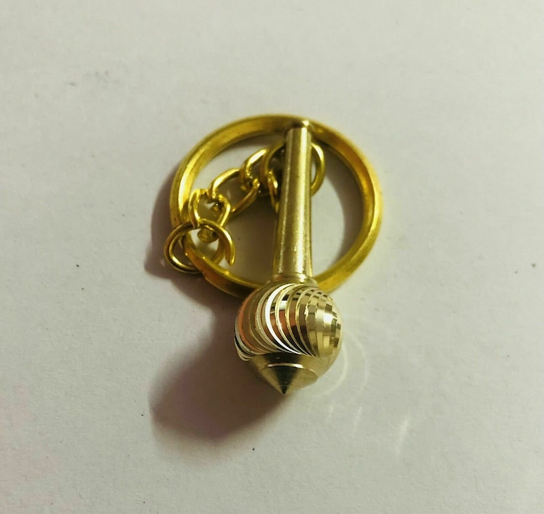 May include: A gold-coloured keychain with a decorative, swirling, pointed ball attached to a ring and chain.