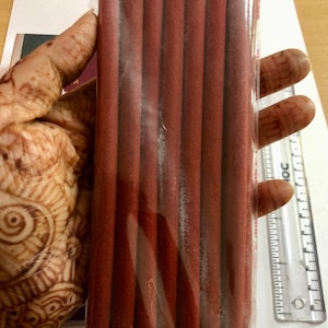 Könnte beinhalten: Eine Packung mit acht braunen Räucherstäbchen, verpackt in durchsichtigem Plastik.