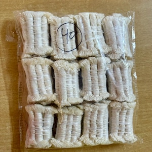 Op de afbeelding: Een doorzichtige plastic zak met meerdere spoelen van crèmekleurige katoenen lonten. De lonten zijn strak opgerold en hebben een gefranjerde rand. Het nummer "40" staat in een cirkel op de zak. De lonten zijn waarschijnlijk voor het maken van kaarsen.