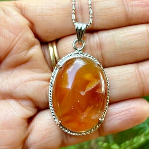 Può includere: Una collana con catena d'argento con un ciondolo ovale che presenta una grande pietra di corniola arancione incastonata in una cornice d'argento.