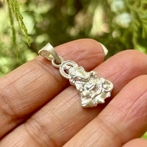 May include: Silver pendant featuring a detailed depiction of the Hindu deity Ganesha. The pendant is designed with a loop for attaching to a chain or cord.
