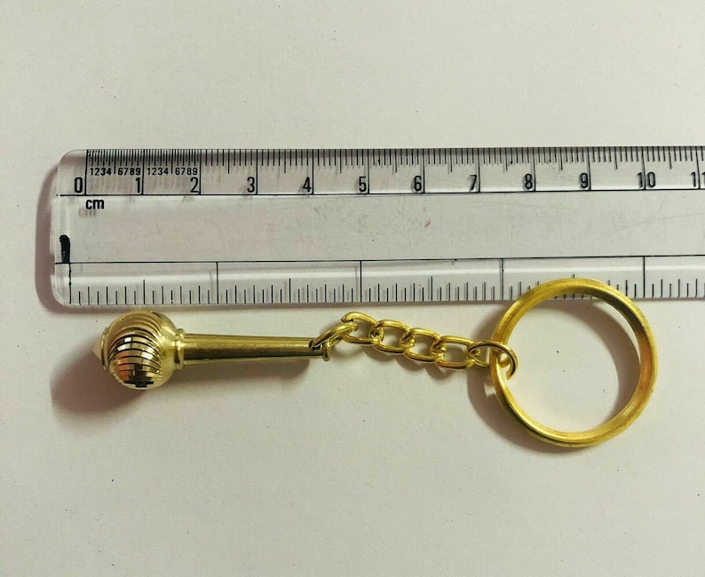 May include: A gold-coloured keychain with a decorative round ornament and a chain attached to a key ring. The ornament has a ribbed design.