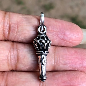 Könnte beinhalten: Ein silberner Anhänger in Form eines stilisierten Zepters mit einer kronenartigen Spitze. Der Anhänger hat komplizierte Details und eine strukturierte Oberfläche.
