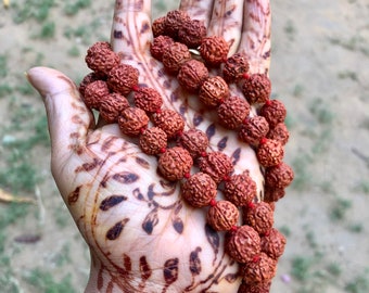 May include: A long strand of brown wooden beads with red string threaded through the beads. The beads are held in a hand with henna.
