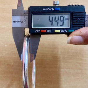 May include: A silver bangle bracelet being measured with a digital caliper. The caliper reads 4.49 mm.