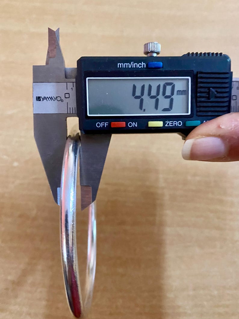 May include: A silver bangle bracelet being measured with a digital caliper. The caliper reads 4.49 mm.