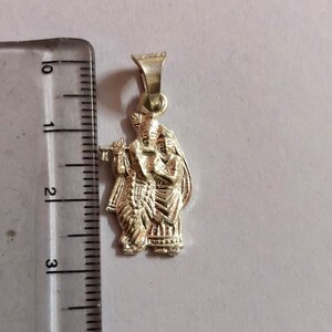 Op de afbeelding: Zilveren hanger met een gedetailleerde afbeelding van Radha Krishna, een hindoe&iuml;stisch godenpaar, waarbij Radha een fluit vasthoudt. De hanger is ongeveer 5 cm hoog.