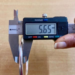 May include: A silver bangle bracelet being measured with a digital caliper. The caliper reads 5.65 mm.
